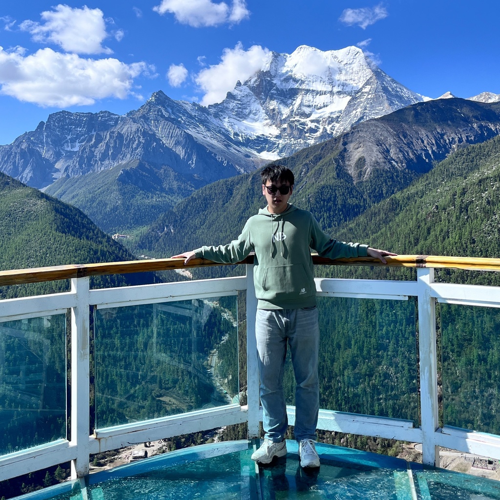 A photo of Xiuchen Jiang standing at an overlook with a mountain range in the background